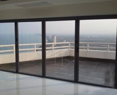 Weather-resistant aluminum folding doors enclosing a high-rise apartment balcony overlooking the city.