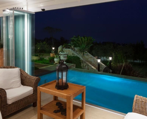 sf25-poolside-terrace-glass-panels-bunched Evening view of a poolside terrace with SF 25 glass panels fully opened and bunched.