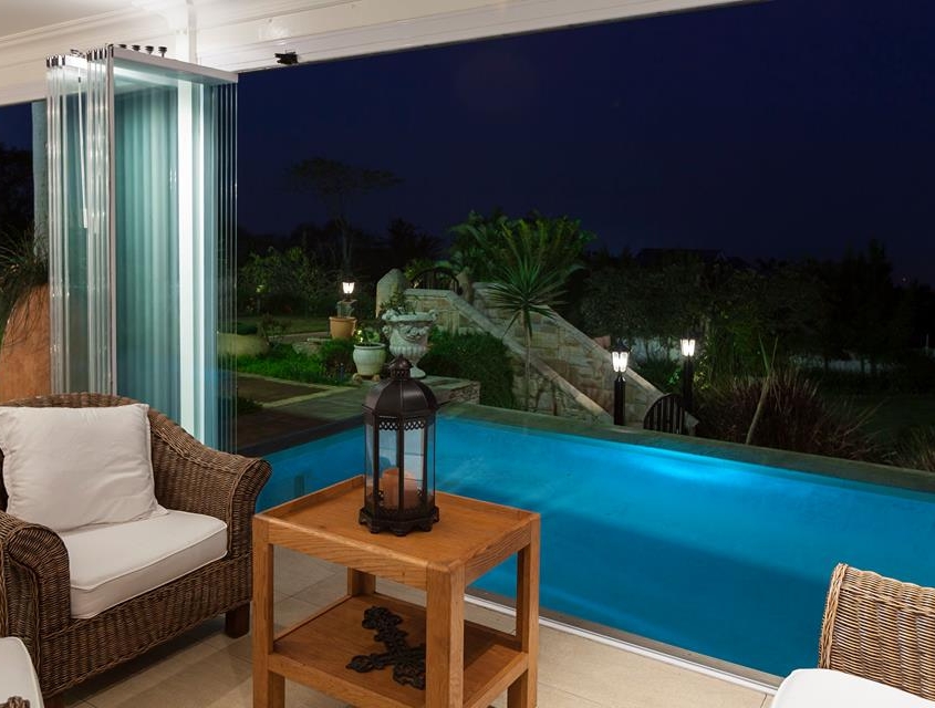 sf25-poolside-terrace-glass-panels-bunched Evening view of a poolside terrace with SF 25 glass panels fully opened and bunched.