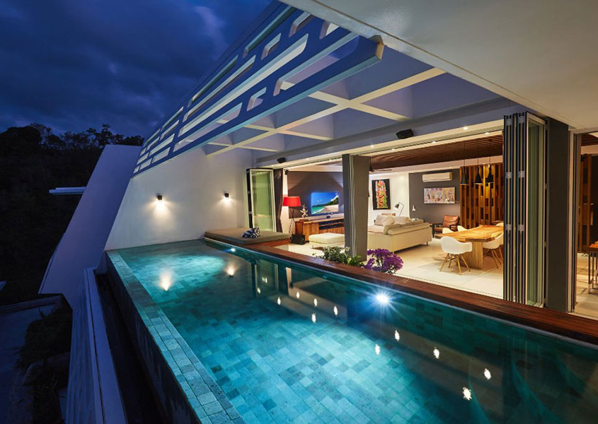 SUNFLEX SF 45 aluminum folding doors opening a modern villa living room to the poolside at night.