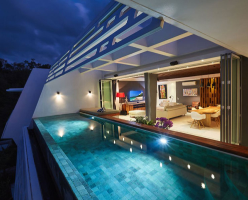 Luxury Thailand villa at night featuring open Sunflex SF 45 aluminium folding doors that seamlessly connect the living room to the private pool area.