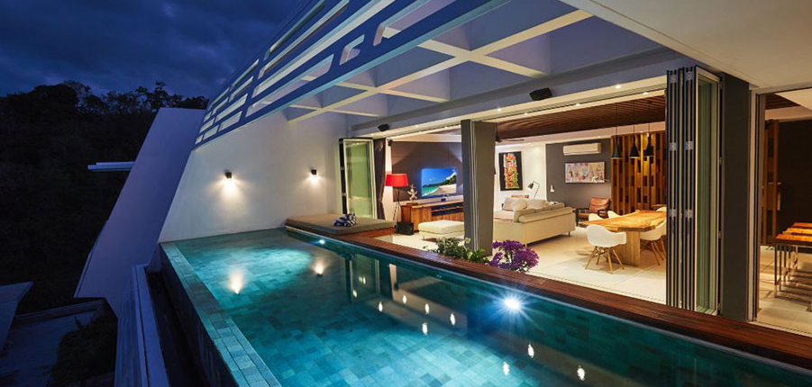 Luxury Thailand villa at night featuring open Sunflex SF 45 aluminium folding doors that seamlessly connect the living room to the private pool area.
