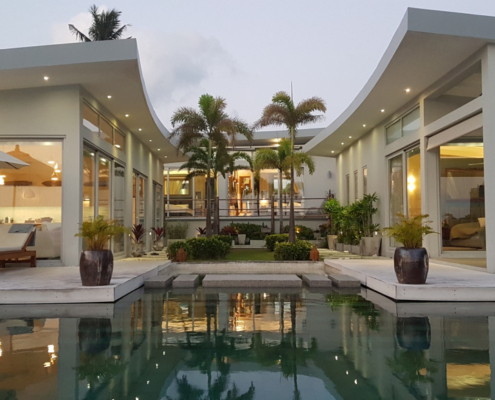 sunflex-sf26-aluminum-sliding-doors-villa-thailand Exterior view of a modern luxury villa in Thailand featuring Sunflex SF 26 aluminum sliding doors by the pool at dusk