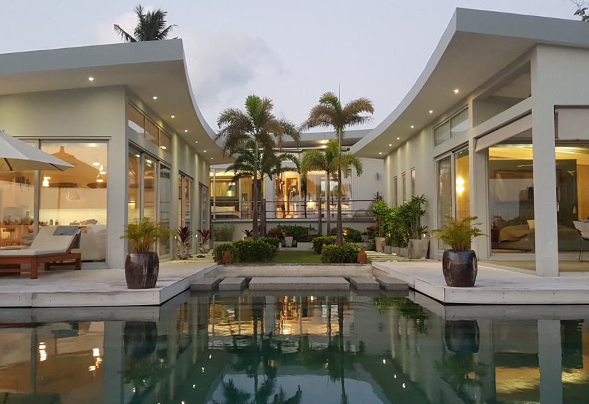 sunflex-sf26-aluminum-sliding-doors-villa-thailand Exterior view of a modern luxury villa in Thailand featuring Sunflex SF 26 aluminum sliding doors by the pool at dusk
