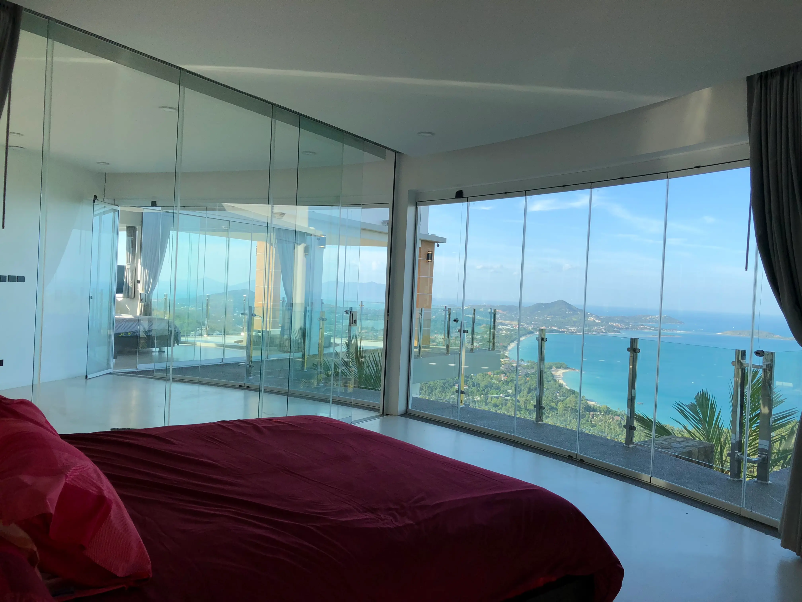 SUNFLEX Asia frameless glass slide and turn system (SF 25) installed on a luxury villa terrace in Koh Samui, Thailand. The closed system offers a 100% unobstructed panoramic view over an infinity pool to the turquoise bay in the Gulf of Thailand, engineered perfectly for coastal, tropical climates.