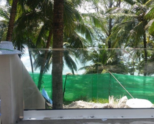 tropical-balcony-railing-palm-trees-thailand Frameless glass balustrade on a balcony with tropical palm trees in Thailand, during luxury development construction.